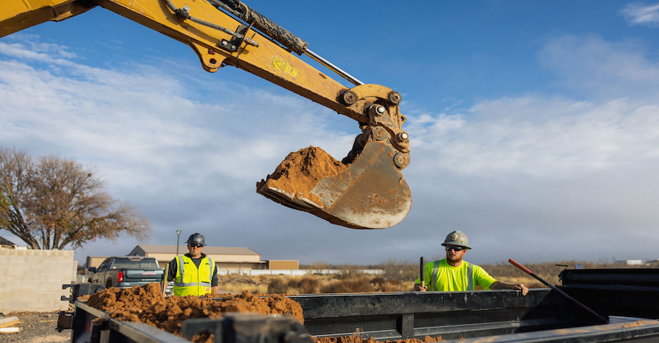 Backhoe scooping dirt into a dump truck