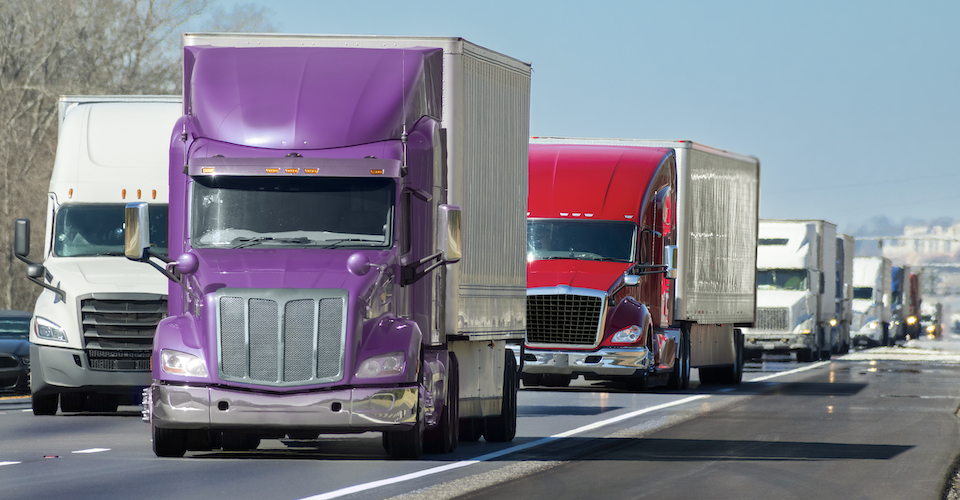 Many semi trucks driving down the road together