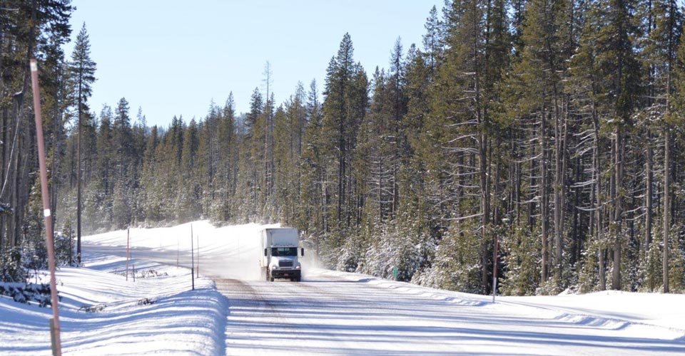 Truck driving down a snowy road with trees lining both sides