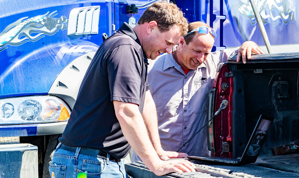 Men looking at a laptop in front of a semi truck